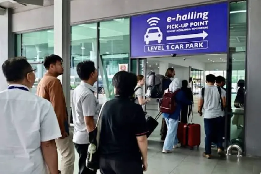 Blue overhead sign reading E-Hailing Pick-Up Point, Level 1 Car Park, with passengers walking beneath it.